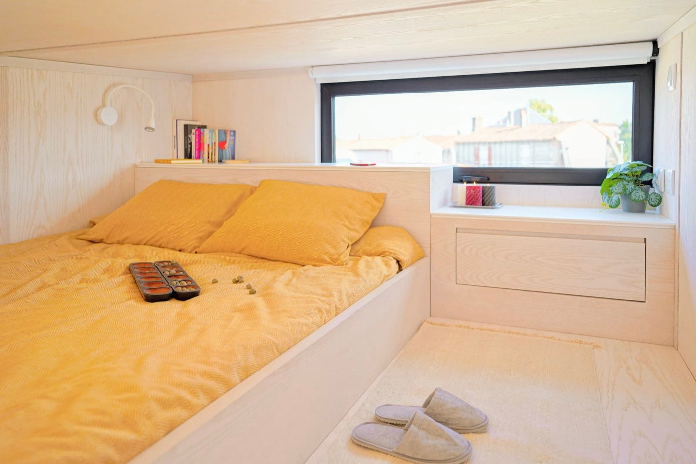 Couchage en alcôve sous la mezzanine, linge ocre et bandeau vitré