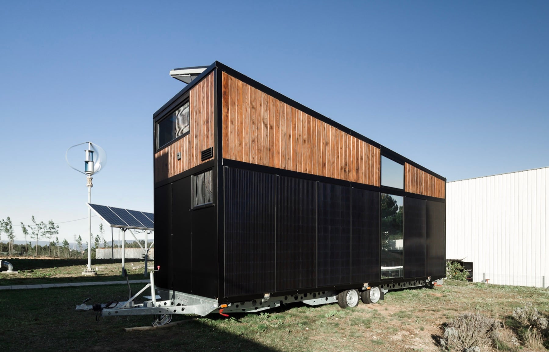 Tiny House Hoummi sur remorque, éolienne et panneaux solaires en arrière-plan