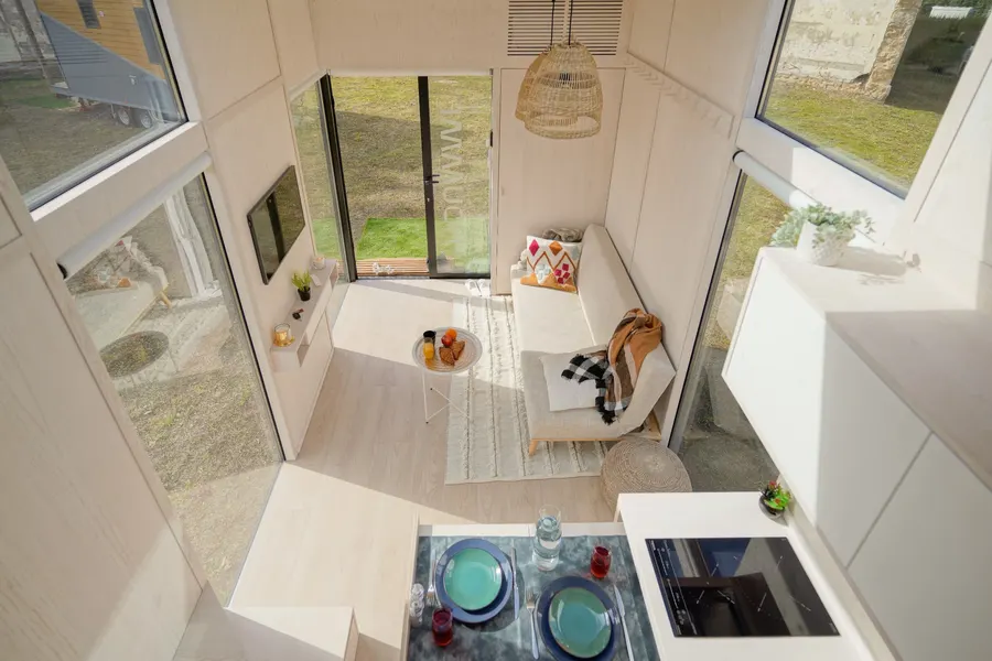 Intérieur d'un module Hoummi vu en plongée : séjour, coin repas dressé et baies vitrées ouvertes sur le jardin