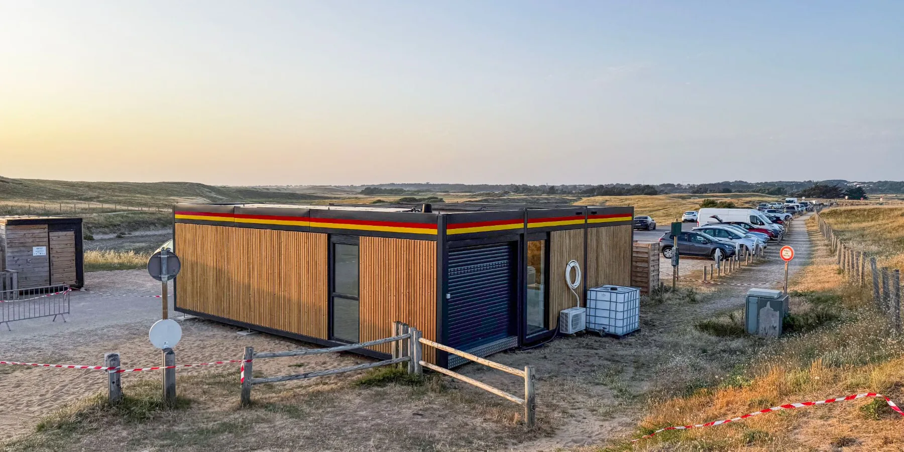 Poste de secours Hoummi de la plage des Granges, aux Sables-d'Olonne, bandeau rouge et jaune, dans les dunes au soleil couchant