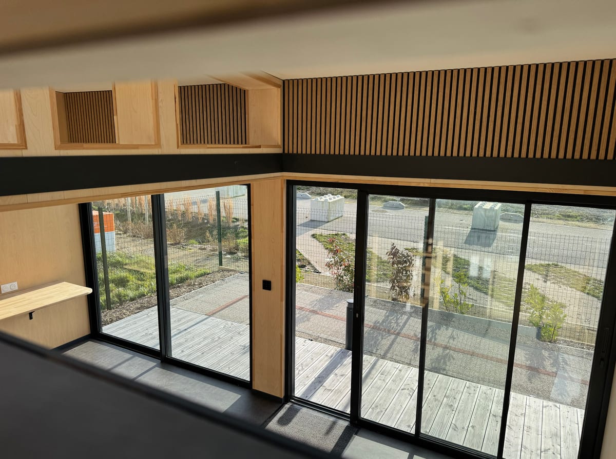 Vue depuis la mezzanine d'un module Hoummi : garde-corps, paroi à tasseaux et baie coulissante sur la terrasse