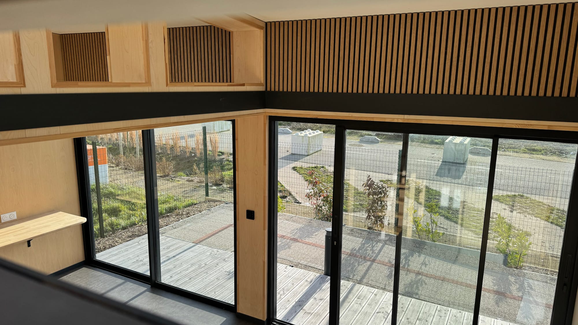 Vue depuis la mezzanine d'un module Hoummi : paroi à tasseaux et baie coulissante sur la terrasse